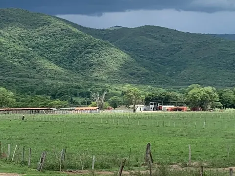Potreros cercados frente a los galpones de la finca, con los cerros detrás bajo un cielo de tormenta.